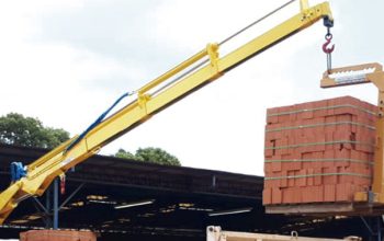 Guindaste veicular realizando carregamento de palete de tijolos em caminhão durante operação logística.
