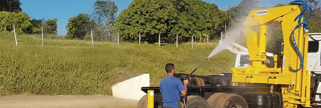 Operador lavando guindaste veicular com jato de pressão durante limpeza e manutenção do equipamento.