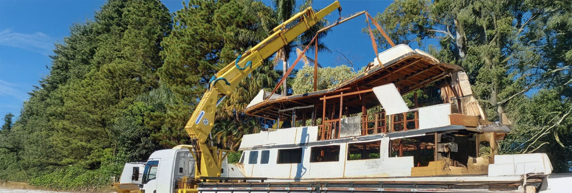 Guindaste veicular içando estrutura de telhado com cintas de amarração durante operação de movimentação de carga.